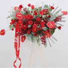 A large, vibrant red floral arrangement with roses, anthuriums, and orchids.