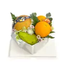 Heart-shaped box of assorted fruits including pear, orange, and green fruit with decorative flowers.