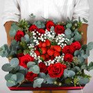 Red roses, strawberries, and baby's breath arranged in a dark box with eucalyptus.