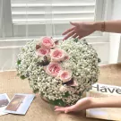 Pink roses and baby's breath in a heart-shaped arrangement, with hands reaching out.