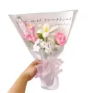 Crocheted bouquet of pink and white flowers wrapped in translucent paper, held by a hand.
