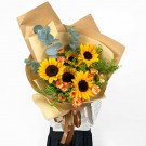 Sunflower bouquet with orange carnations and eucalyptus leaves, wrapped in brown paper.