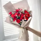 Bouquet of red roses with white filler flowers, wrapped in beige paper and tied with a cream ribbon.