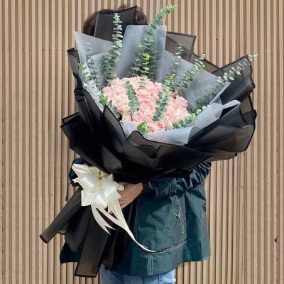 A large bouquet of pink roses and eucalyptus, wrapped in black and light gray paper with a white ribbon.