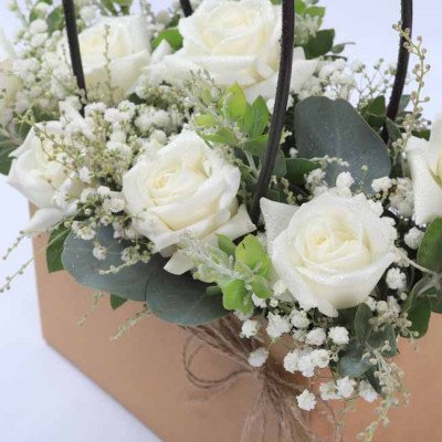 White roses, baby's breath, and eucalyptus in a brown box with twine.