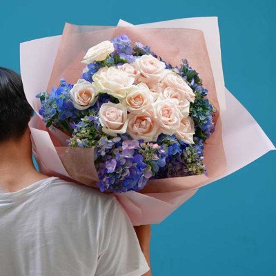 Man carrying a bouquet of white and pink roses with blue hydrangeas.