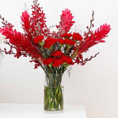 Vase of red carnations, ginger, and orchid flowers against a white background.
