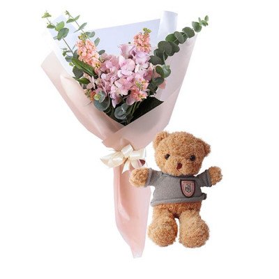Bouquet of pink flowers and a teddy bear in a grey sweater.