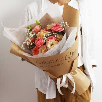 A bouquet of pink roses, lisianthus, and baby's breath wrapped in brown paper, with "Gorgeous You" printed on it.