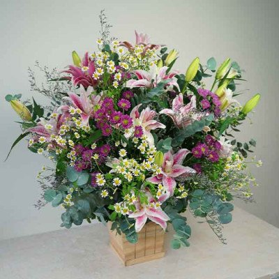 Wood box of pink lilies, daisies, and green leaves