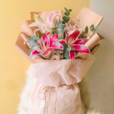 Bouquet of pink and white lilies with eucalyptus, wrapped in brown and white paper, tied with twine.