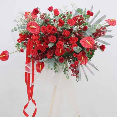 A large, vibrant red floral arrangement with roses, anthuriums, and orchids.