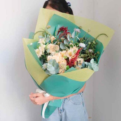 Woman holding a pastel bouquet wrapped in green and yellow paper.