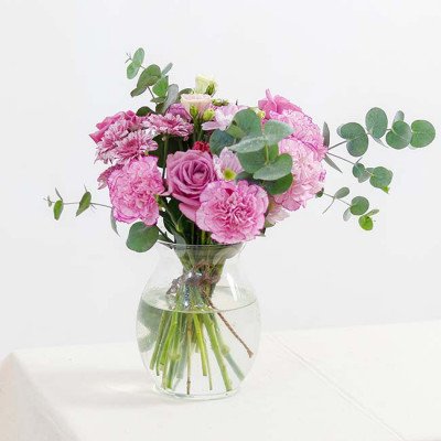 Pink and purple flowers in a glass vase with eucalyptus leaves.