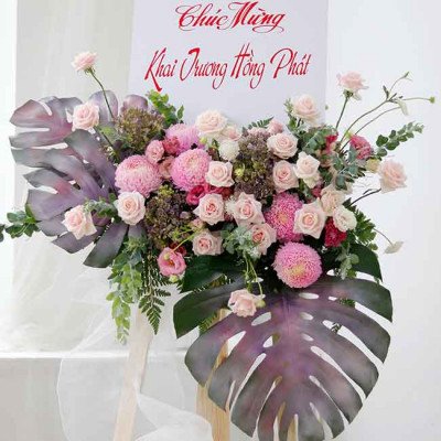 A flower arrangement with pink roses, chrysanthemums, and monstera leaves on a white banner.