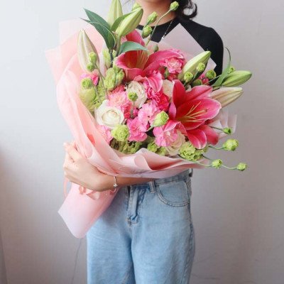 Woman holding a bouquet of pink lilies, roses, and carnations wrapped in pink paper.