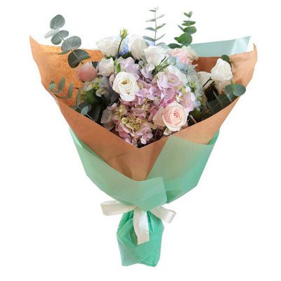 Pastel flower bouquet with roses, lisianthus, hydrangeas, and eucalyptus in brown and green paper wrap.
