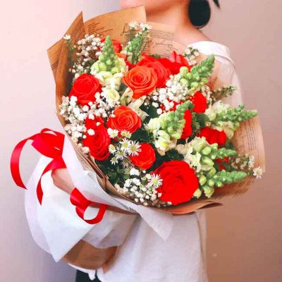 Vibrant bouquet of red roses, snapdragons, and baby's breath with a red ribbon.