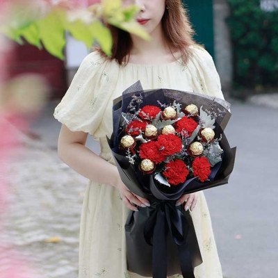 Woman in yellow dress holding a bouquet of red carnations and Ferrero Rocher chocolates.