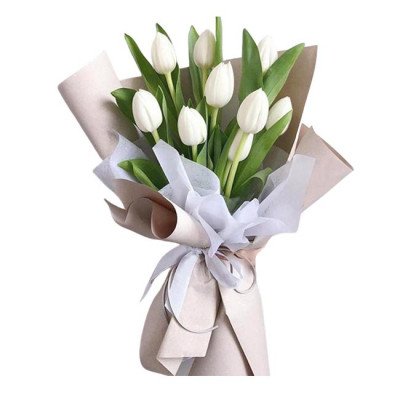 A bouquet of white tulips with green leaves, wrapped in brown and white paper, tied with a white ribbon.