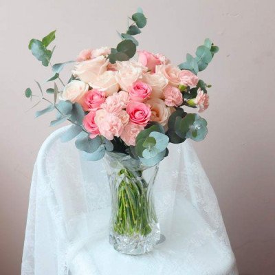 A bouquet of pink and cream roses with eucalyptus leaves in a clear glass vase.