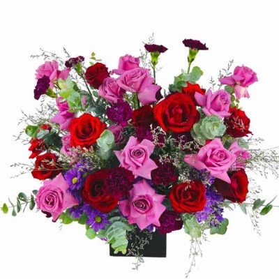 A vibrant floral arrangement of red and pink roses, purple carnations, and other greenery in a black box.