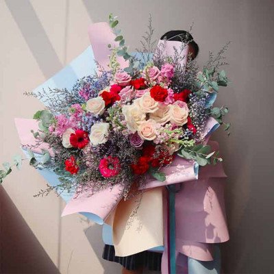 A lush bouquet of pink, red, and cream roses with various other flowers and greenery, wrapped in pastel paper.