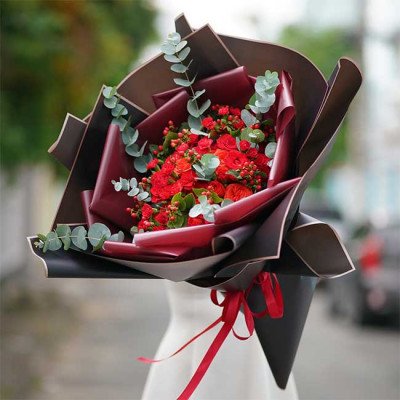 Bouquet of red roses and carnations with eucalyptus leaves, wrapped in dark brown and red paper.