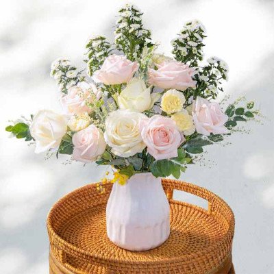 A bouquet of pink and white roses with yellow accents in a white vase.