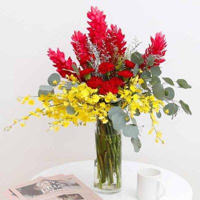 Red ginger, yellow dancing orchids, red carnations, and eucalyptus in a glass vase.