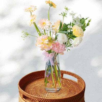 Vase of light pink and yellow spring flowers with a pink ribbon.