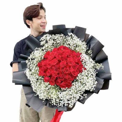 Man holding a large bouquet of 99 red roses and baby's breath.