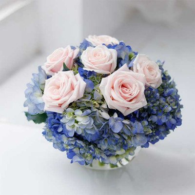 Pink roses and blue hydrangeas in a round vase.