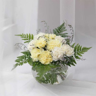 Yellow and white carnations with ferns in a clear glass bowl.