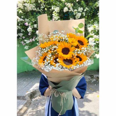 Bouquet of sunflowers and baby's breath flowers wrapped in brown paper and green fabric.