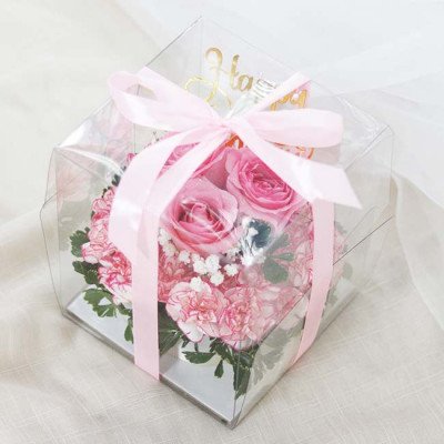 Pink rose and carnation cake in a clear box, tied with a pink ribbon, with a "Happy Birthday" topper.