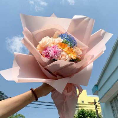 Bouquet of pink roses, blue hydrangea, and yellow daisies wrapped in pink paper.