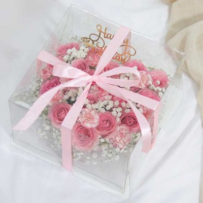 Pink rose and carnation cake in a clear box with pink ribbon and "Happy Birthday" banner.