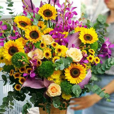 A wooden gift box filled with sunflowers, roses, orchids, and greenery.