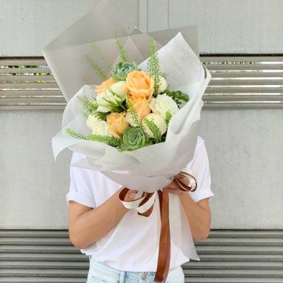 A bouquet of peach and white roses, succulents, and greenery, tied with a brown ribbon.