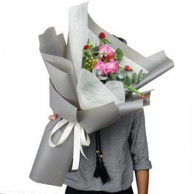 Pink roses and other flowers in a gray and white bouquet, tied with a white ribbon.