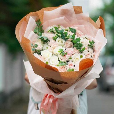 A bouquet of pink and white roses, carnations, and greenery, wrapped in brown paper.