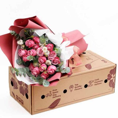 Pink rose bouquet in pink and red wrapping, on top of a cardboard box with floral designs.