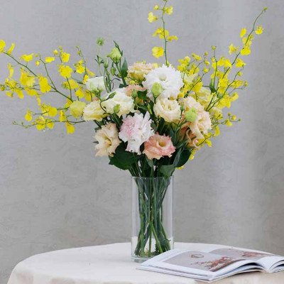 A clear glass vase holds a bouquet of yellow dancing lady orchids and pastel roses.