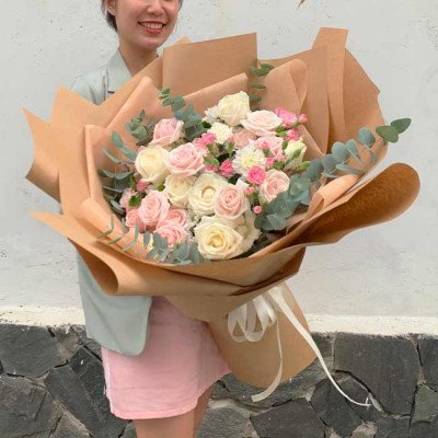 A woman holds a large bouquet of pink and white roses wrapped in brown paper.