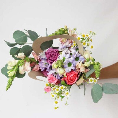 A vibrant bouquet of roses, daisies, snapdragons, and eucalyptus in a brown paper holder.