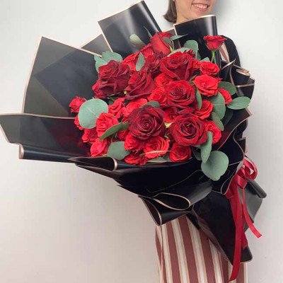 Large bouquet of deep red roses with dark wrapping and red ribbon.