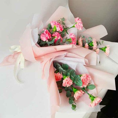 Pink carnations and eucalyptus bouquet wrapped in pink and white paper, tied with a cream ribbon.