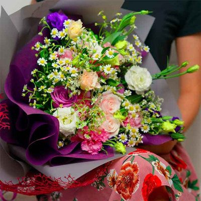 A bouquet of pink, white, and purple flowers with daisies, wrapped in purple paper.