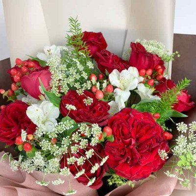 Red Ohara roses and white Freesias in a bouquet, accented with berries and greenery.
